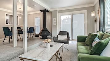 Uma sala de estar moderna com lareira, sofá verde e um espaço de jantar com cadeiras.