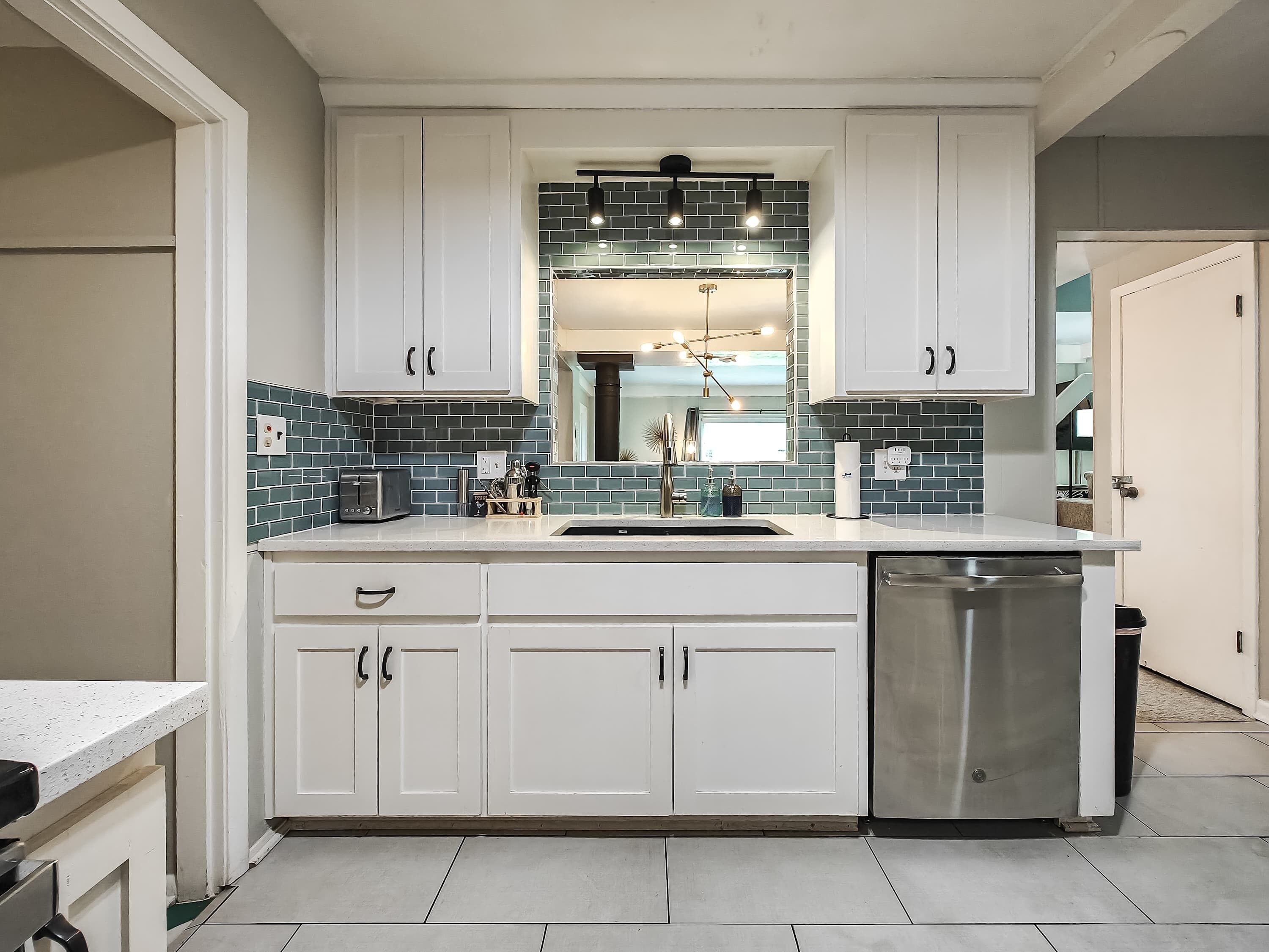 Una cocina moderna con armarios blancos, un lavavajillas de acero inoxidable y un protector de salpicaduras de azulejos.