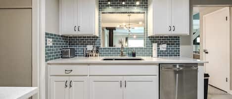 Una cocina moderna con armarios blancos, un lavavajillas de acero inoxidable y un protector de salpicaduras de azulejos.