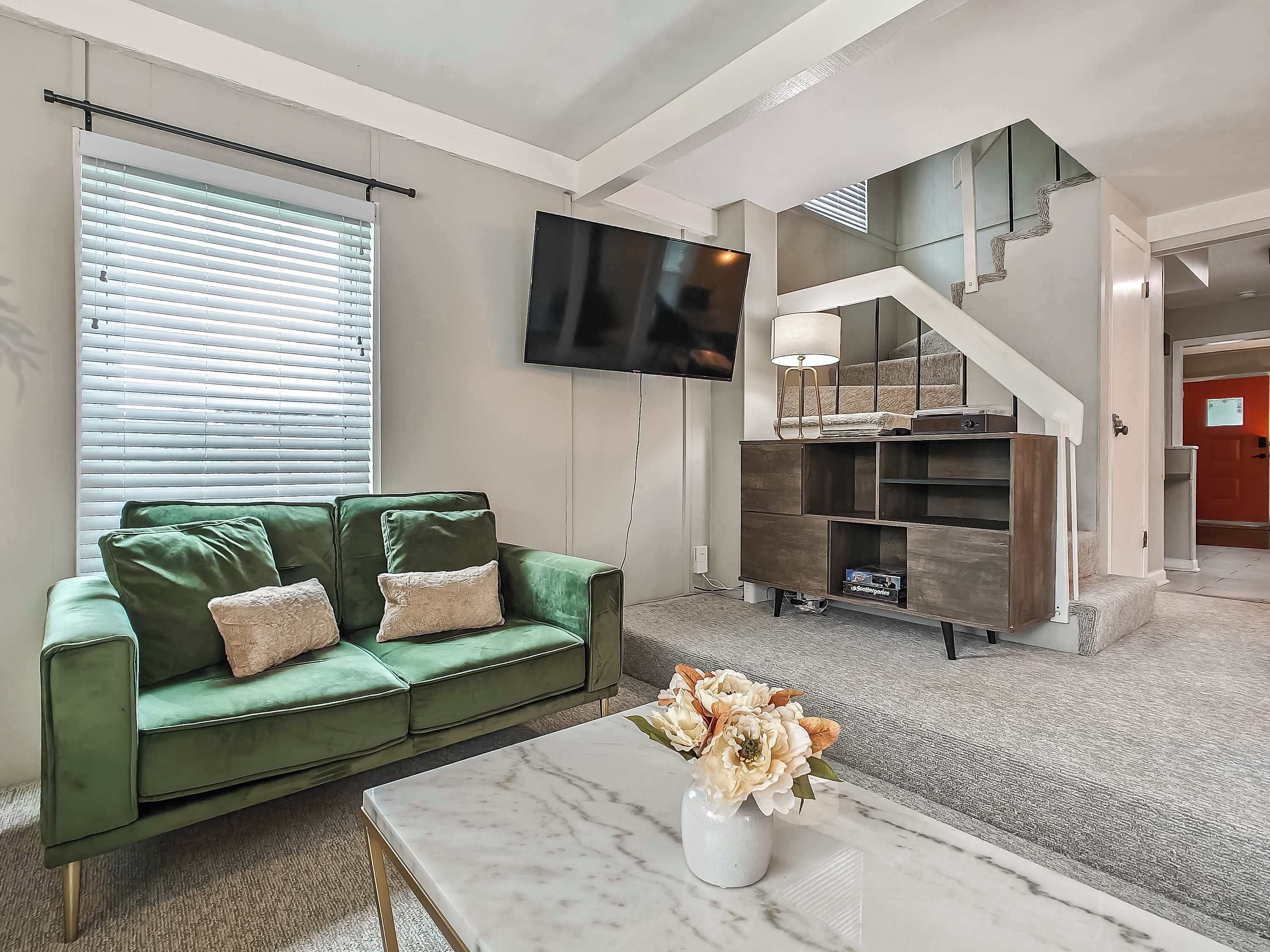 Uma sala de estar moderna com um sofá verde, uma televisão de tela plana, uma mesa de centro de mármore e uma escada com design exclusivo.