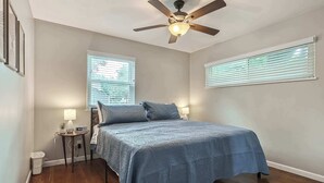 A bedroom with a bed, a ceiling fan, two bedside tables with lamps, and a window with blinds. - 4 Bdrm Getaway with Hot Tub (Overland Park)