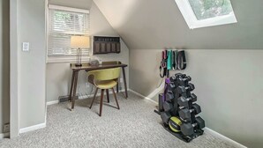 A room with a sloped ceiling, a desk with a chair, a lamp, a radiator, and a wall-mounted dumbbell rack. - 4 Bdrm Getaway with Hot Tub (Overland Park)