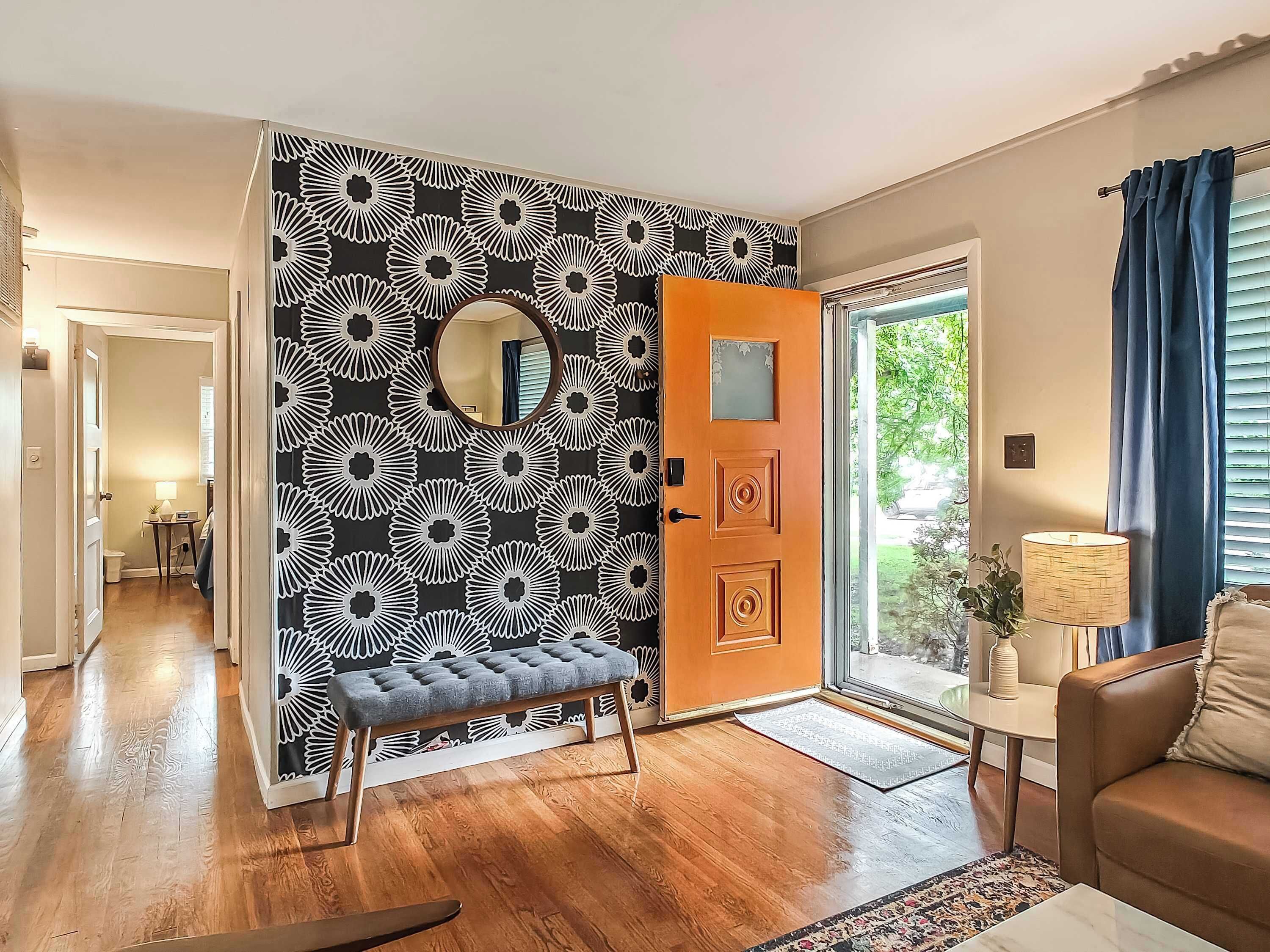 A living room with a wooden bench, a round mirror, and a patterned wall.
