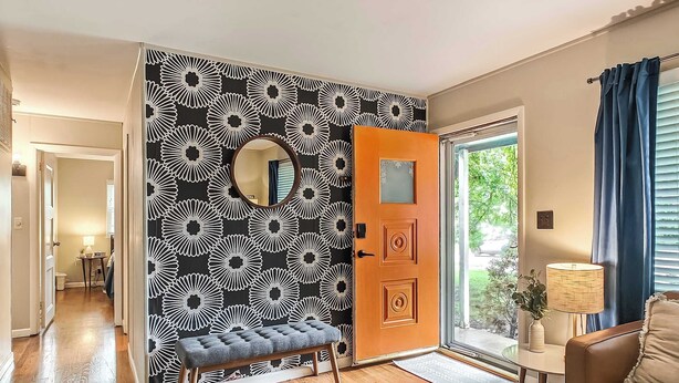 A living room with a wooden bench, a round mirror, and a patterned wall. - 4 Bdrm Getaway with Hot Tub (Overland Park)
