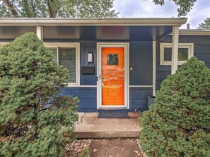 Una casa de color azul con una puerta naranja brillante y un pequeño porche con un felpudo negro.