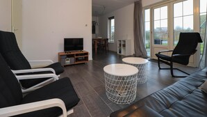 Een moderne woonkamer met een bank, twee fauteuils, een televisie en een eethoek met een tafel en stoelen.