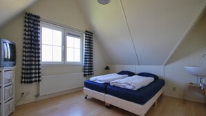 Een slaapkamer met een bed, een televisie, een raam met gordijnen, een radiator en een lamp.