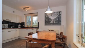 Een moderne keuken met een houten eettafel en stoelen, een hangende lamp en een stadslandschap op de muur.