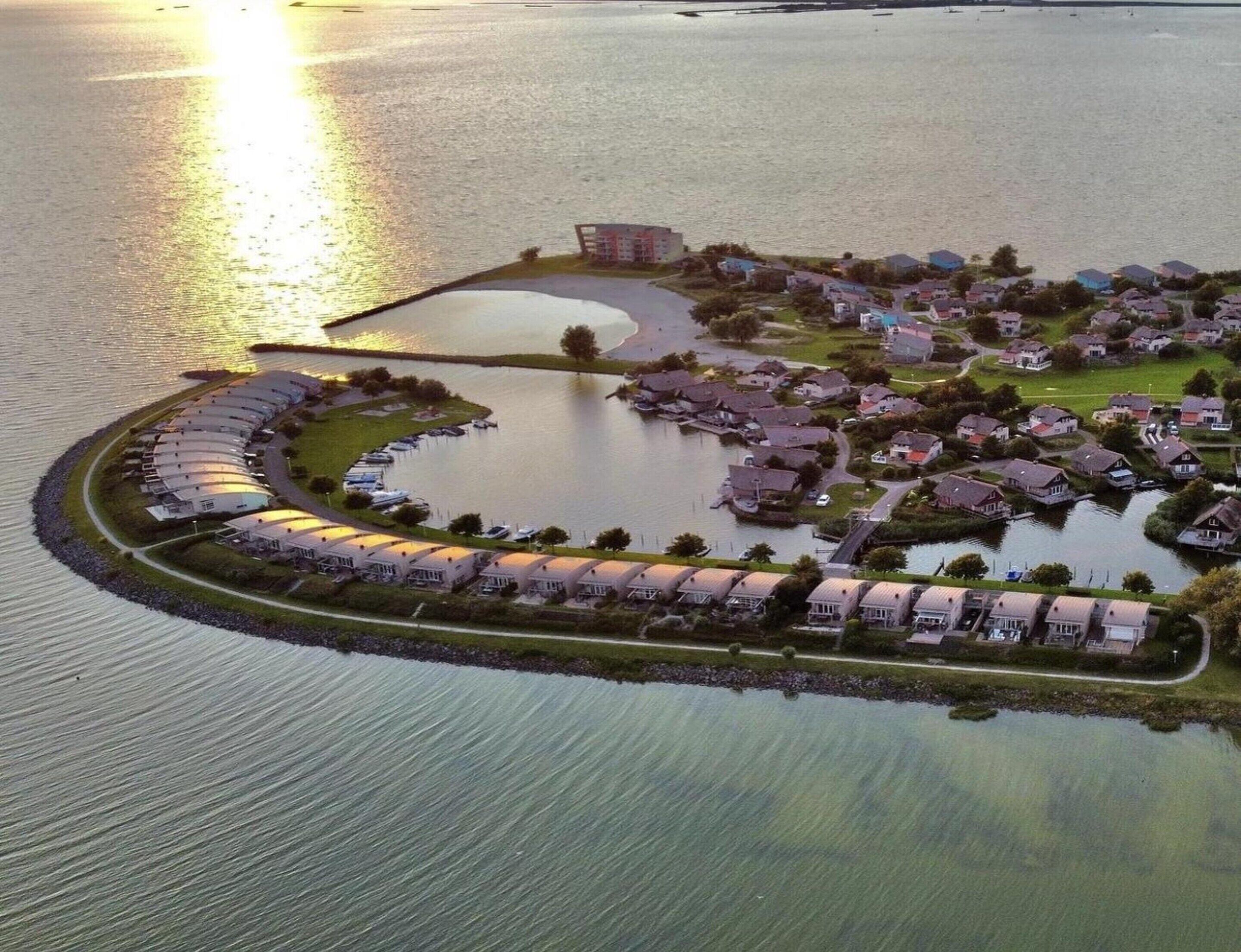 A waterfront property with a crescent-shaped building complex, a marina with boats, and a residential area with houses.