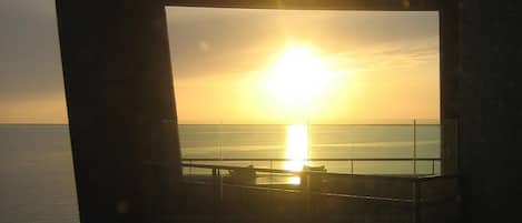 A balcony with a view of the sunset over the ocean.