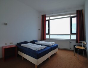 Una habitación con dos camas, una silla, una mesita y una ventana con cortinas.