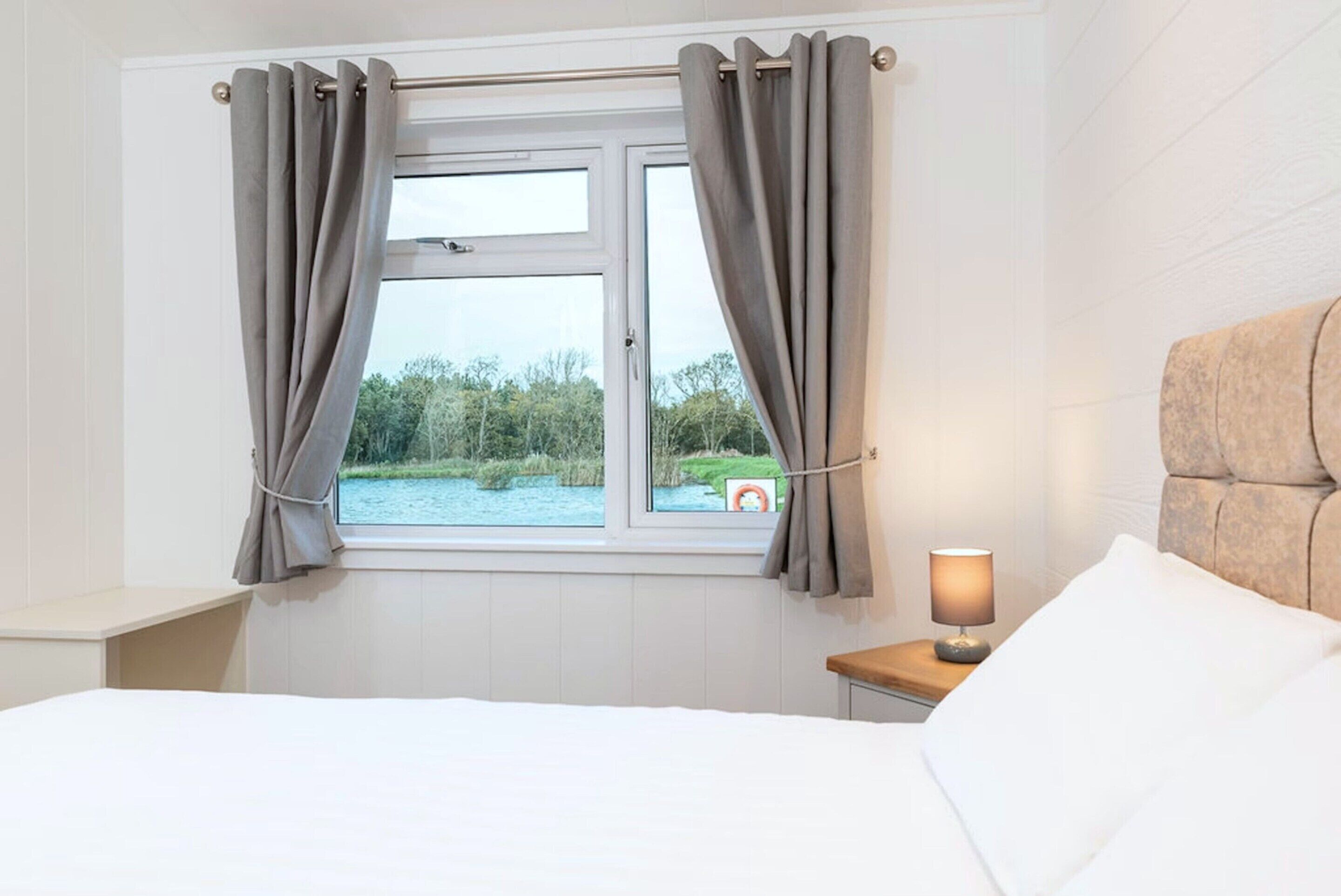 A bedroom with a bed, a nightstand, a lamp, and a window with curtains.