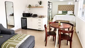 Ein kompaktes Hotelzimmer mit Küchenzeile, Essbereich, Bett und einem großen Spiegel.
