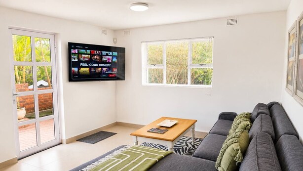 Ein modernes Wohnzimmer mit einem grauen Sofa, einem Holztisch und einem flachbildfernseher an der Wand.