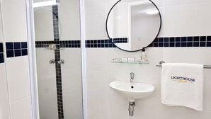 Ein Badezimmer mit einer gläsernen Duschkabine, einem weißen Waschbecken und einem Handtuchhalter mit einem Handtuch mit der Aufschrift 'LIGHTHOUSE Suite'.