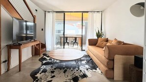 Un salon moderne comprenant un canapé, une table basse, un téléviseur posé sur un meuble et un coin repas avec des chaises et une table.