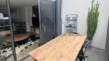 An outdoor patio with a wooden table and chairs, a metal chair, a potted cactus, and a metal shelf with containers.