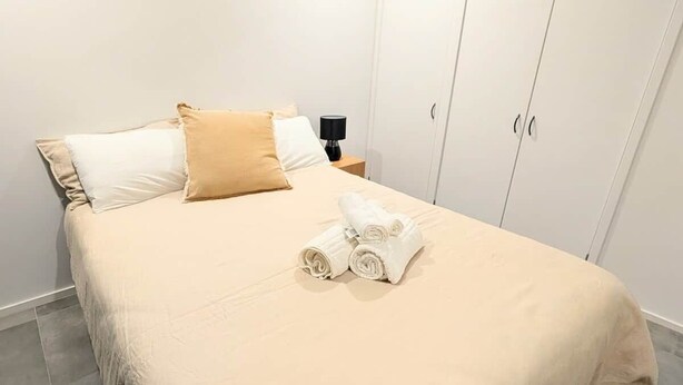 Un lit bien fait, recouvert d’une couvre-lit beige, avec deux oreillers et des serviettes enroulées posées sur le lit.