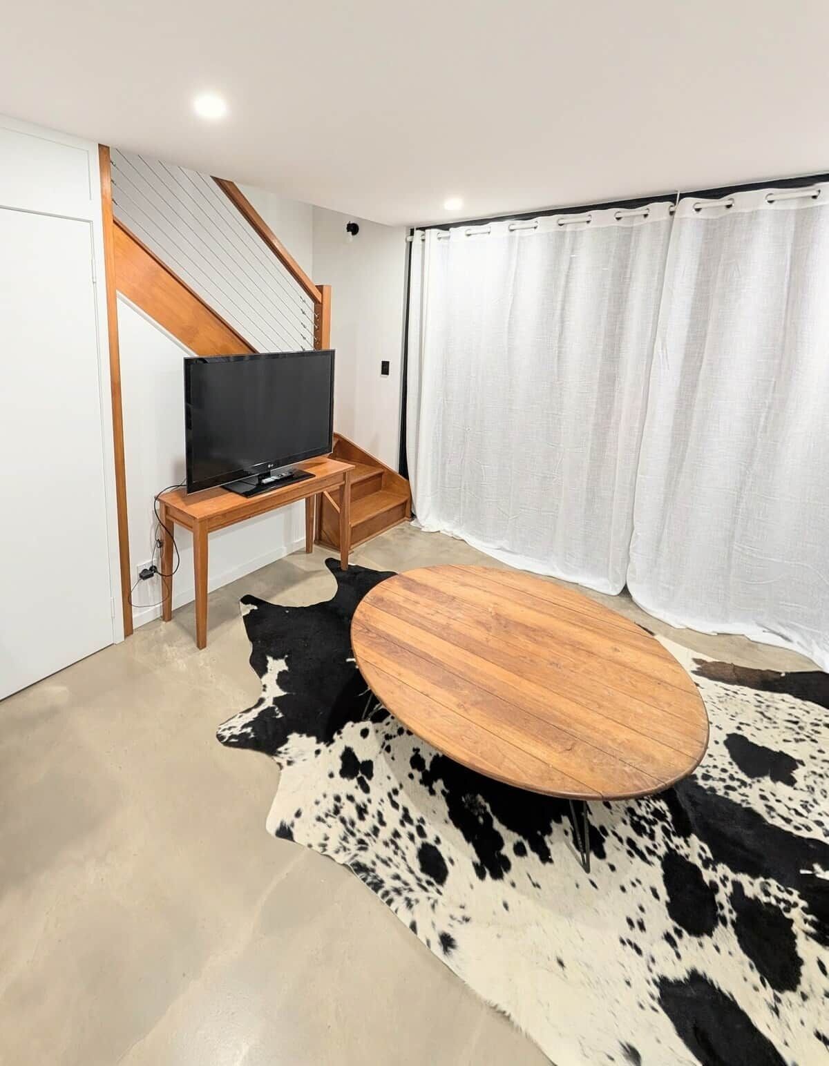 A modern living room with a flat-screen TV on a wooden stand, a round wooden coffee table, and a black and white cowhide rug.