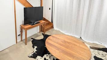 A modern living room with a flat-screen TV on a wooden stand, a round wooden coffee table, and a black and white cowhide rug.