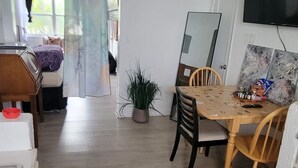 Et værelse med et træbord, stole, en potteplante, et fjernsyn og en seng med gardin.