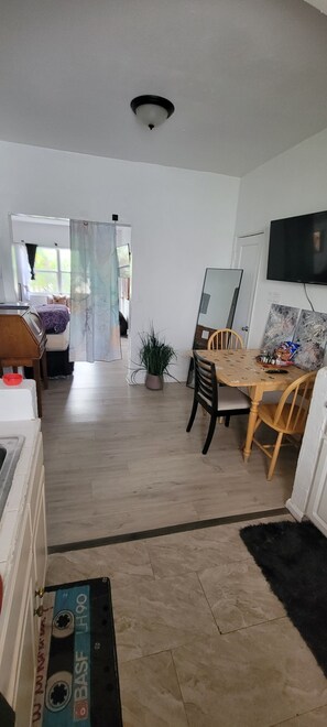 Una habitación con una mesa de comedor de madera, sillas, una planta en maceta, un televisor y una cama con cortina.