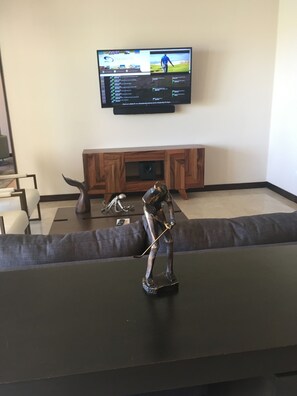 A living room with a television mounted on the wall, a wooden entertainment unit below, and a sculpture on a table. - Posh 2-bedroom condo in charming Cabo with AC, kitchen and 2.5 baths.Ocean view. (Cabo San Lucas)