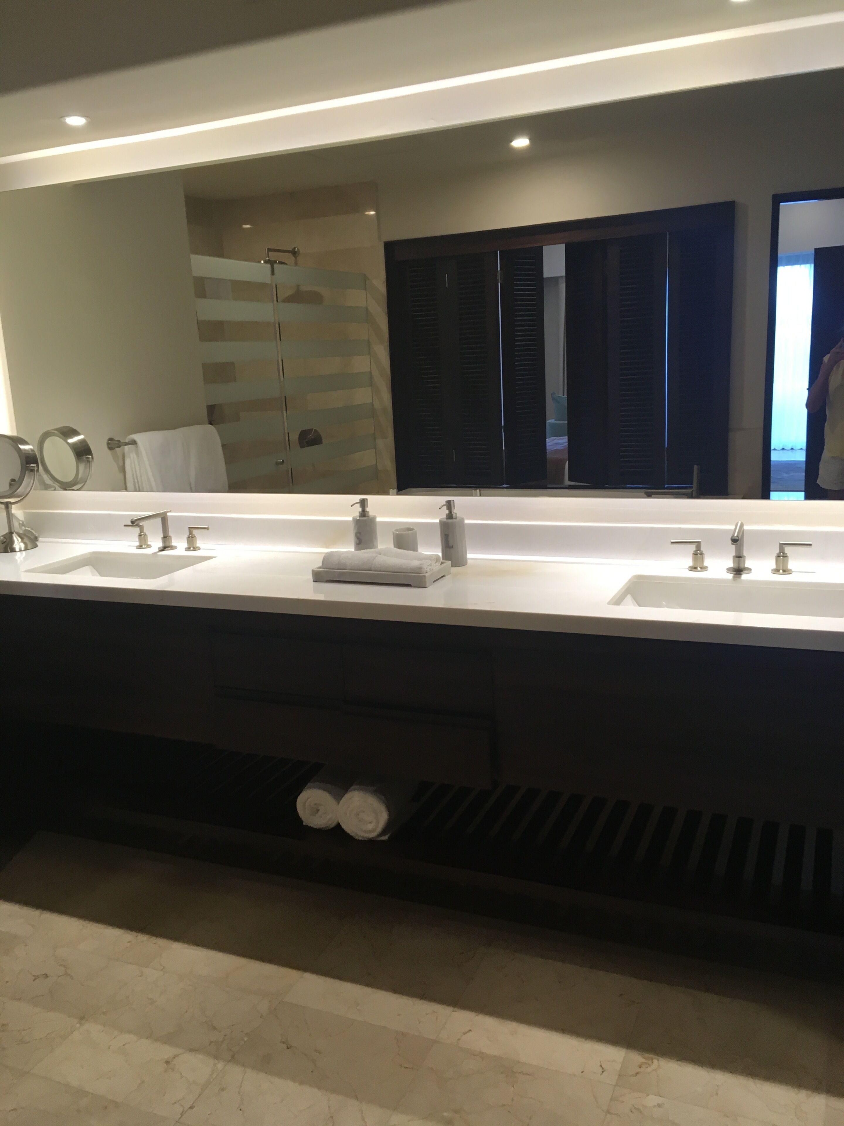 A bathroom with a large mirror, two sinks, and a towel rack.