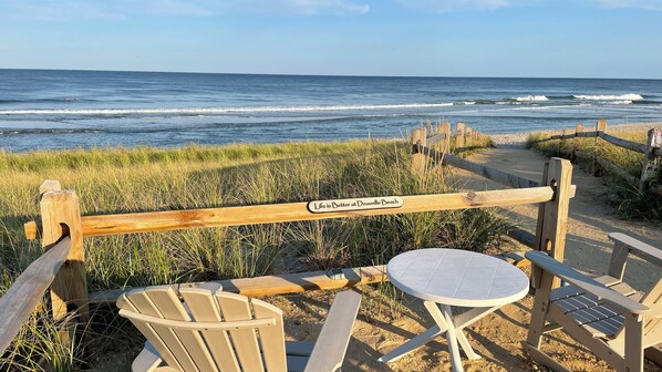 A beachside seating area with a table and chairs, a wooden fence with a sign, and the ocean in the background. - Perfect Peaceful Shore Getaway! Close to beach, private yard, off street parking (Mantoloking)