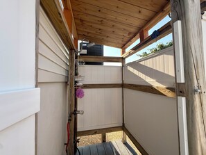 Eine Holzterrasse mit weißem Zaun, einem Metallgestell und einer violetten Blume.