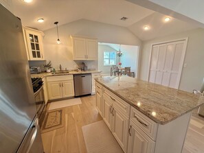 A kitchen with white cabinets, a granite countertop, a dishwasher, and a dining area with a table and chairs. - Perfect Peaceful Shore Getaway! Close to beach, private yard, off street parking (Mantoloking)