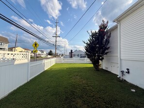 A residential area with a white fence, a grassy yard, and houses in the background. - Perfect Peaceful Shore Getaway! Close to beach, private yard, off street parking (Mantoloking)