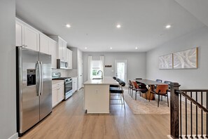 A modern kitchen with stainless steel appliances, a dining area with a long table and chairs, and a staircase leading to another level. - Exquisitely finished 3-bedroom Townhome on 3-levels with 2-car garage. (Glenarden)