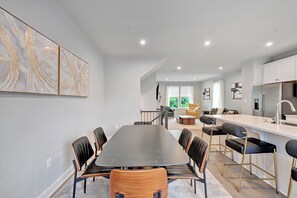 A modern kitchen with a dining area, featuring a long table and chairs, a bar area, and a view of the outdoors. - Exquisitely finished 3-bedroom Townhome on 3-levels with 2-car garage. (Glenarden)