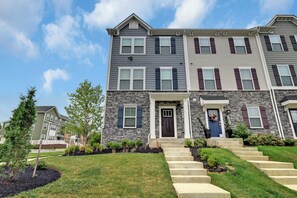 A multi-story residential building with a stone facade, a front entrance with steps, and a clear sky. - Exquisitely finished 3-bedroom Townhome on 3-levels with 2-car garage. (Glenarden)