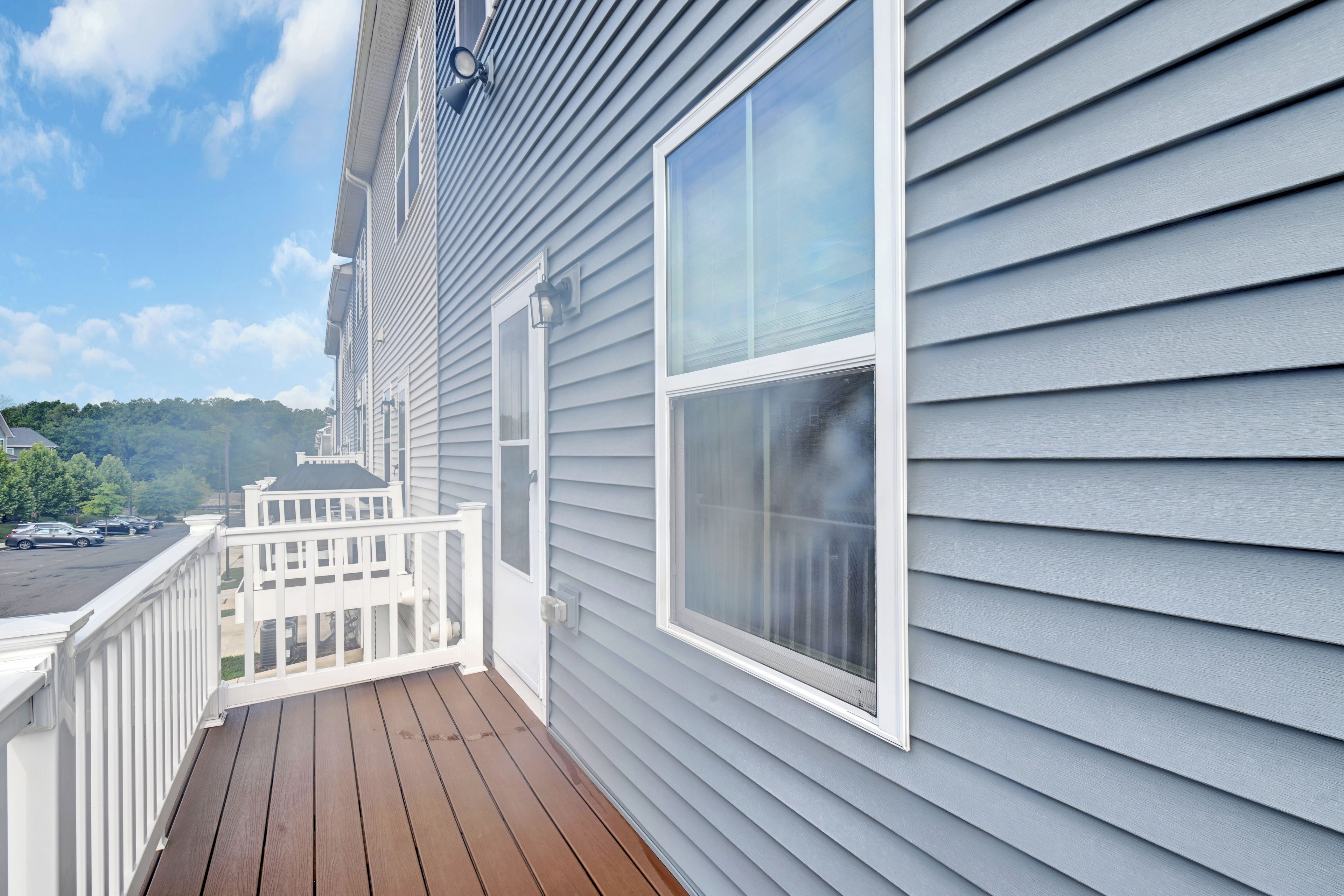 Un immeuble résidentiel doté d’une terrasse en bois, de balustrades blanches et d’une grande fenêtre.
