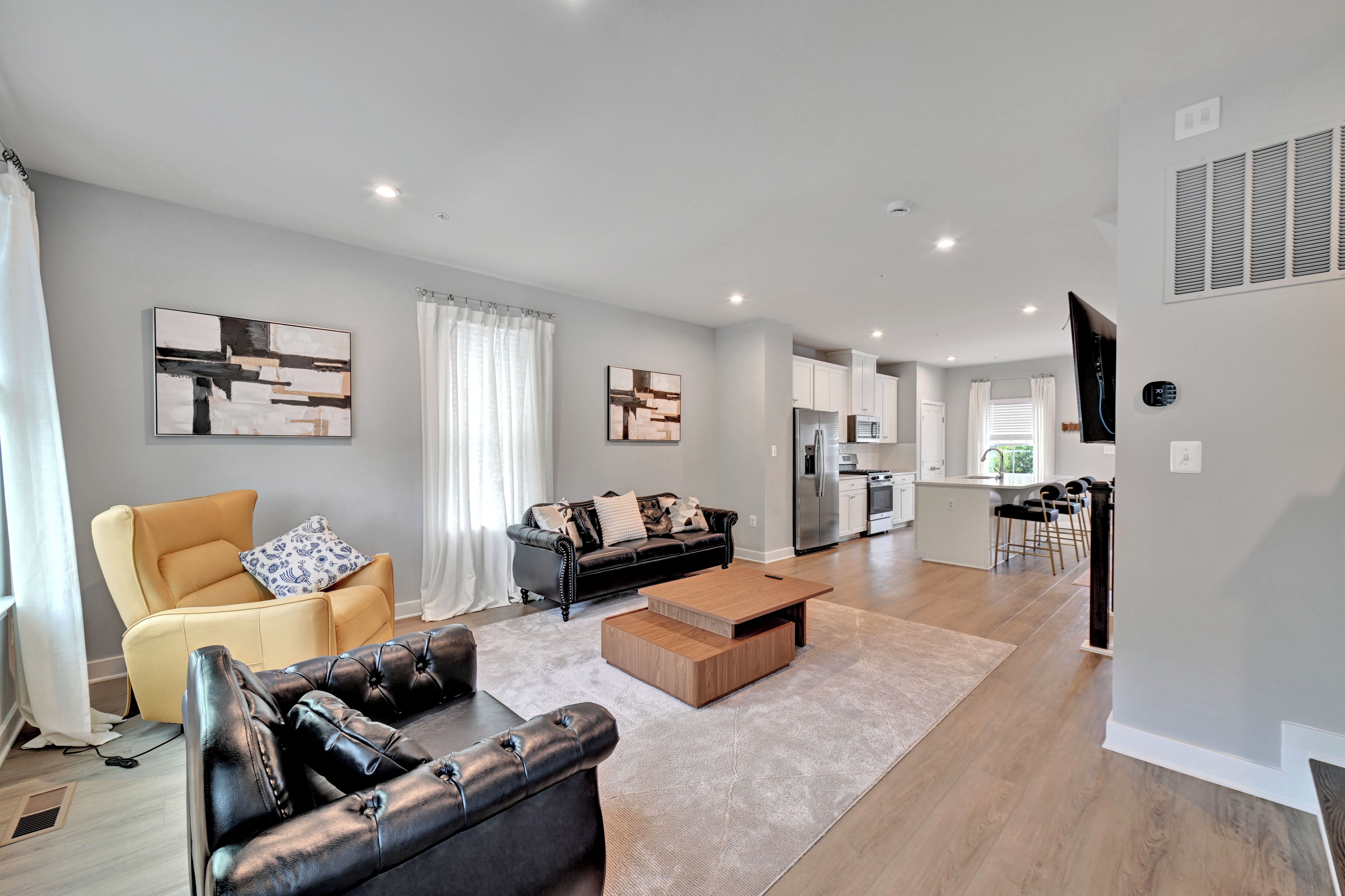 Un salon moderne comprenant un canapé, un fauteuil et une table basse, une cuisine équipée et un coin repas avec des chaises.