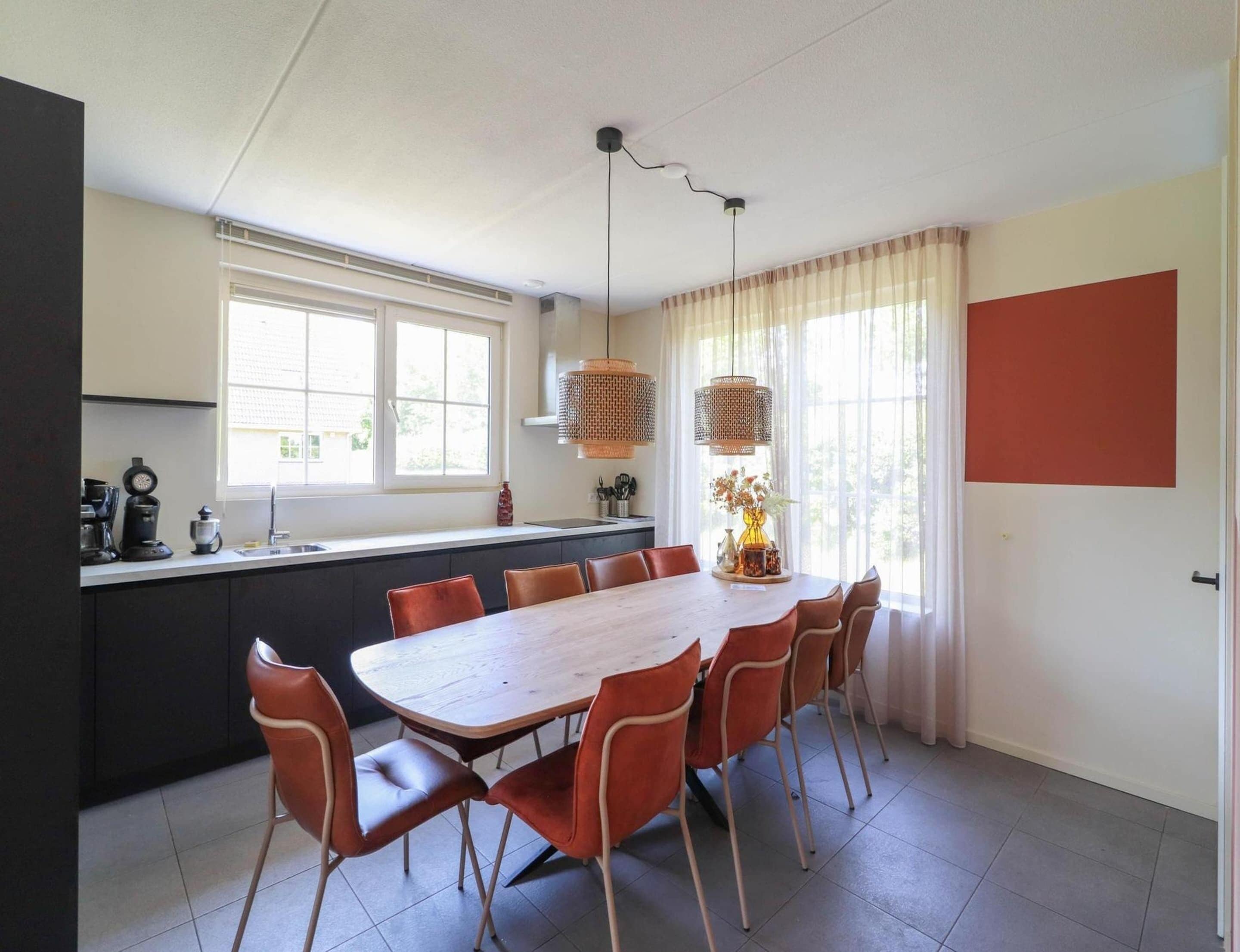 A modern kitchen with a dining area featuring a wooden table and chairs, a window with curtains, and a hanging light fixture.