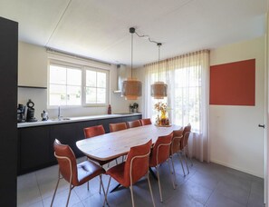 A modern kitchen with a dining area featuring a wooden table and chairs, a window with curtains, and a hanging light fixture. - Luxury Beach Villa With Hot Tub (Makkum)