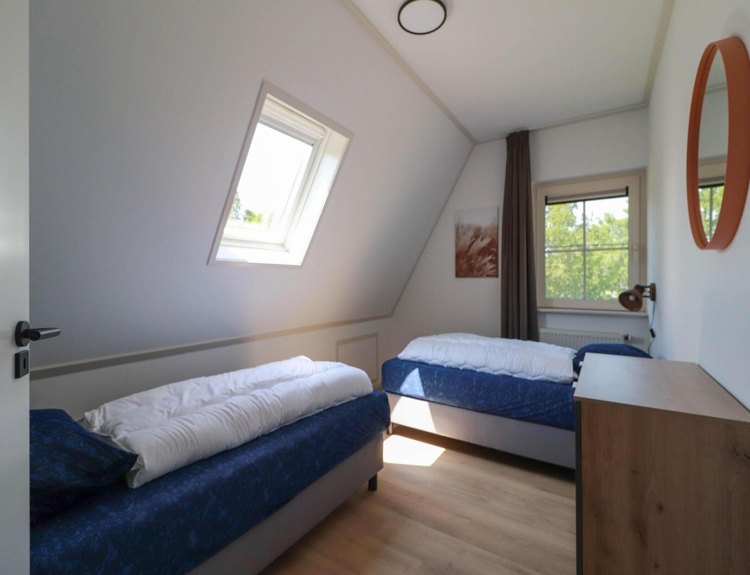 A room with two beds, a skylight, a window, and a wooden dresser.