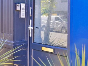 A door with a keypad lock, a handle, and a window with a view of parked cars and a tree. - Charming Apartment in Rhos on Sea (Colwyn Bay)