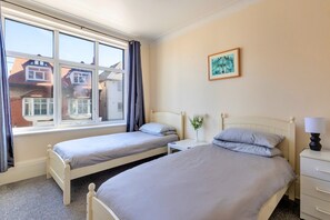 A bedroom with two single beds, a bedside table with a lamp, a small bedside table with a vase of flowers, and a framed picture on the wall. - Charming Apartment in Rhos on Sea (Colwyn Bay)
