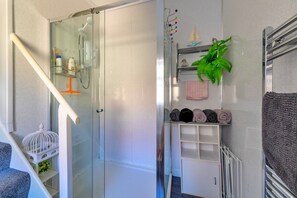 A bathroom with a glass shower enclosure, a white towel rack with towels, and a small plant. - Charming Apartment in Rhos on Sea (Colwyn Bay)