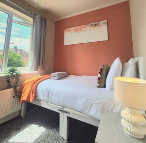 A hotel room with a bed, a bedside lamp, a window with curtains, and a painting on the wall. - Family 3BR Home | Free Parking | Near City Centre (Birstall)