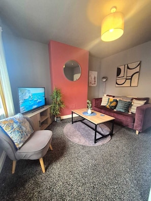 A living room with a sofa, a coffee table, a TV, a mirror, and a plant. - Family 3BR Home | Free Parking | Near City Centre (Birstall)