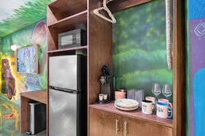 Une cuisine équipée d’un réfrigérateur, d’un four à micro-ondes, d’une machine à café et ornée d’une fresque murale.