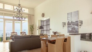 A spacious living area with a sofa, dining table, and chairs, a chandelier, a clock, and a framed picture on the wall. - Panoramic Villa With Sauna & Lake Views (Makkum)