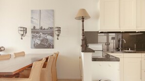 A dining area with a table and chairs, a kitchen with cabinets and a stove, and wall-mounted lighting fixtures. - Panoramic Villa With Sauna & Lake Views (Makkum)