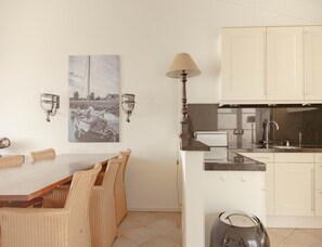 A dining area with a table and chairs, a kitchen with cabinets and a stove, and wall-mounted lighting fixtures. - Panoramic Villa With Sauna & Lake Views (Makkum)