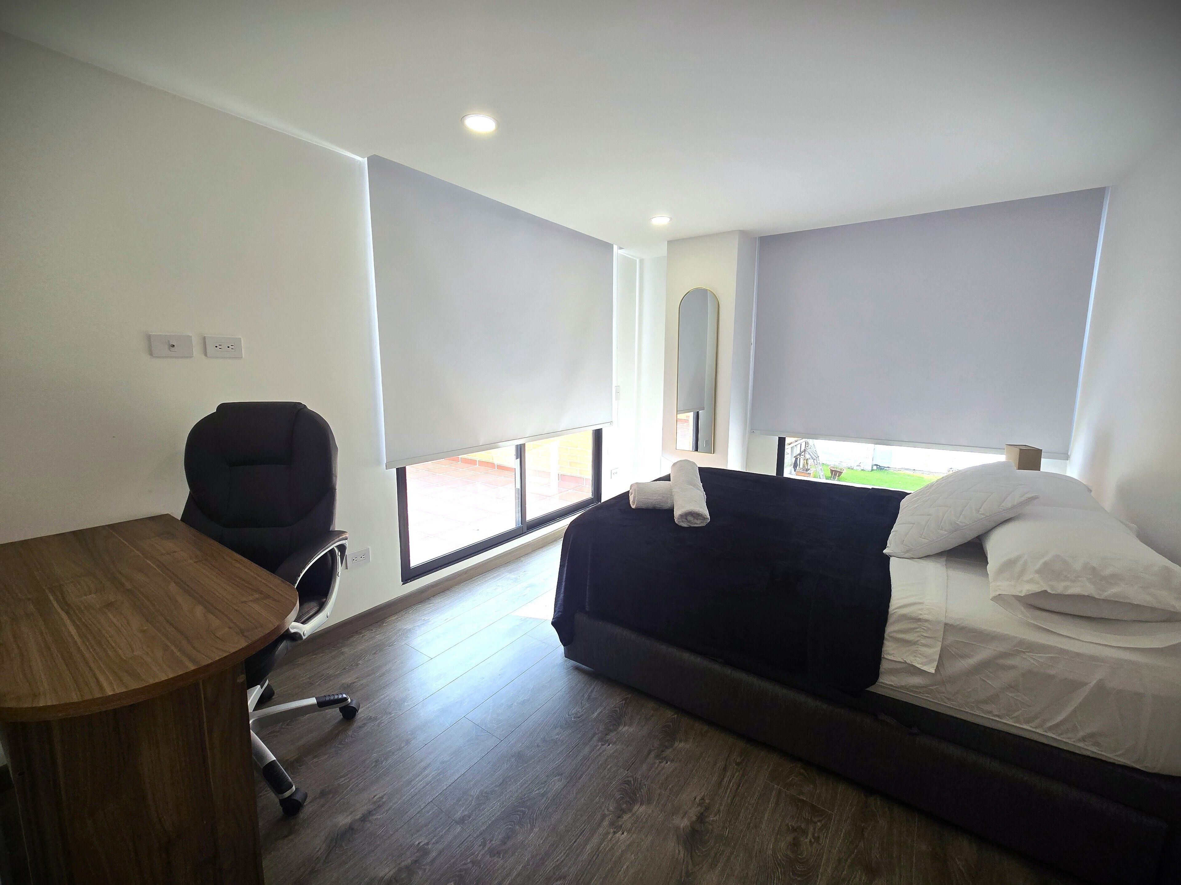 Een kamer met een bed, een bureau, een stoel en een raam.